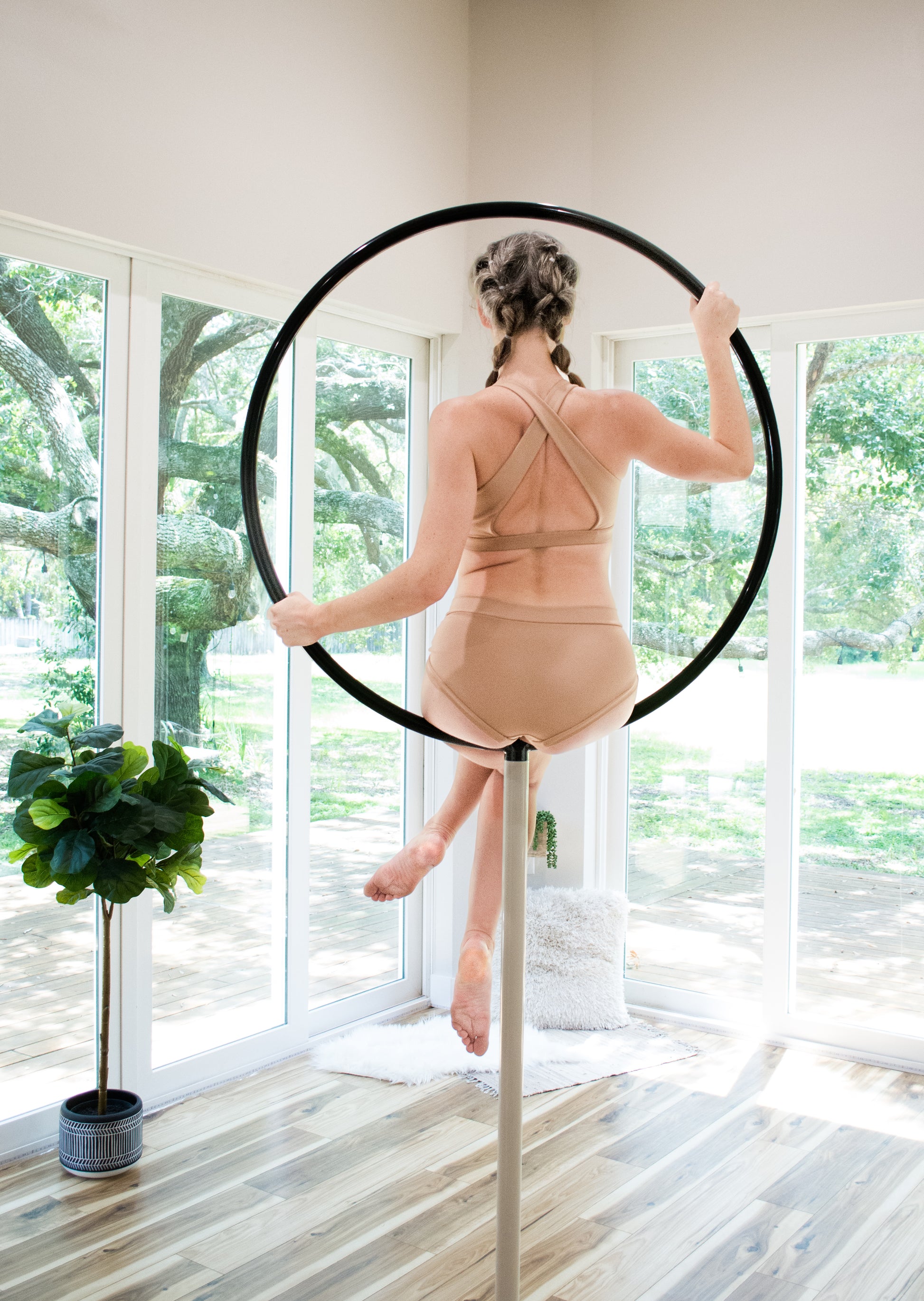 Model in a back view wearing a nude colored pole dance set sitting on a lollipop lyra